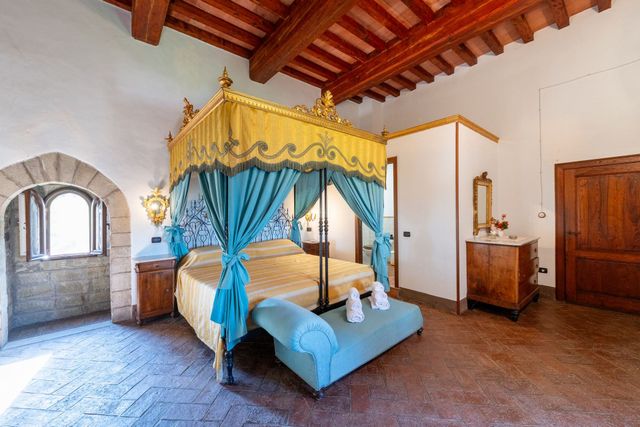Letto a baldacchino con tende blu in una camera da letto rustica con travi in ​​legno a vista e pareti in pietra.