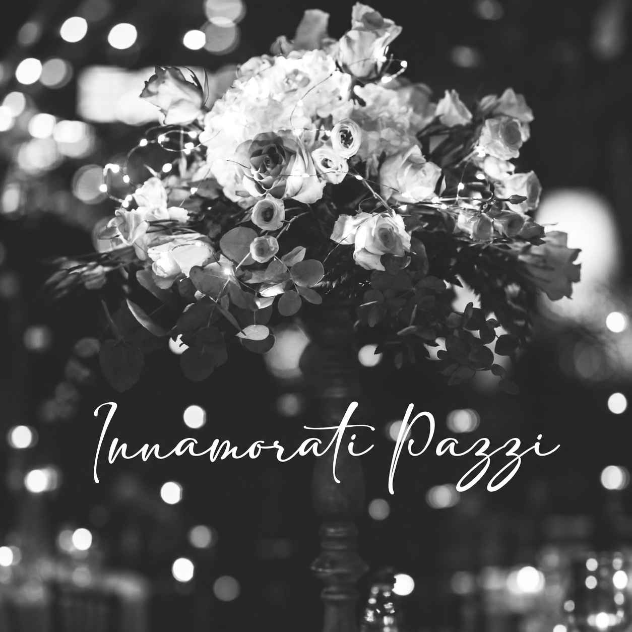 Black-and-white floral bouquet on a stand with “Innamorati Pazzi” text over a blurred lights background