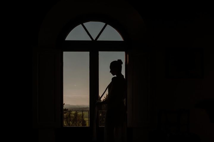 Silhouette di una persona in piedi accanto a una porta, che guarda un paesaggio illuminato dal tramonto.