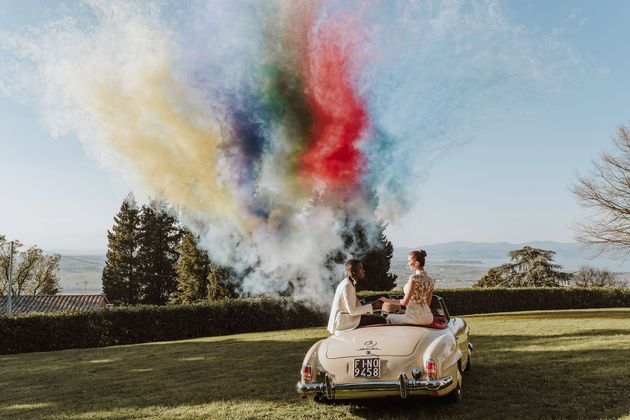 Couple releasing colorful smoke from a convertible on a grassy overlook