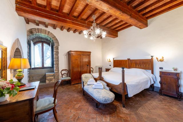 Camera da letto rustica con soffitto con travi in ​​legno, lampadario, letto, armadio e finestra in pietra.
