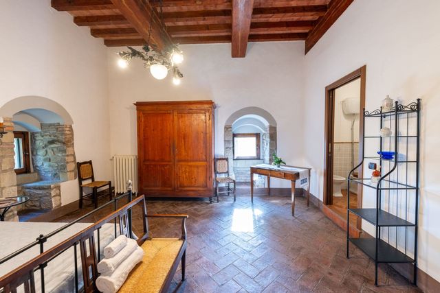 Camera rustica con travi in ​​legno, finestre ad arco, pavimento piastrellato e mobili vintage.