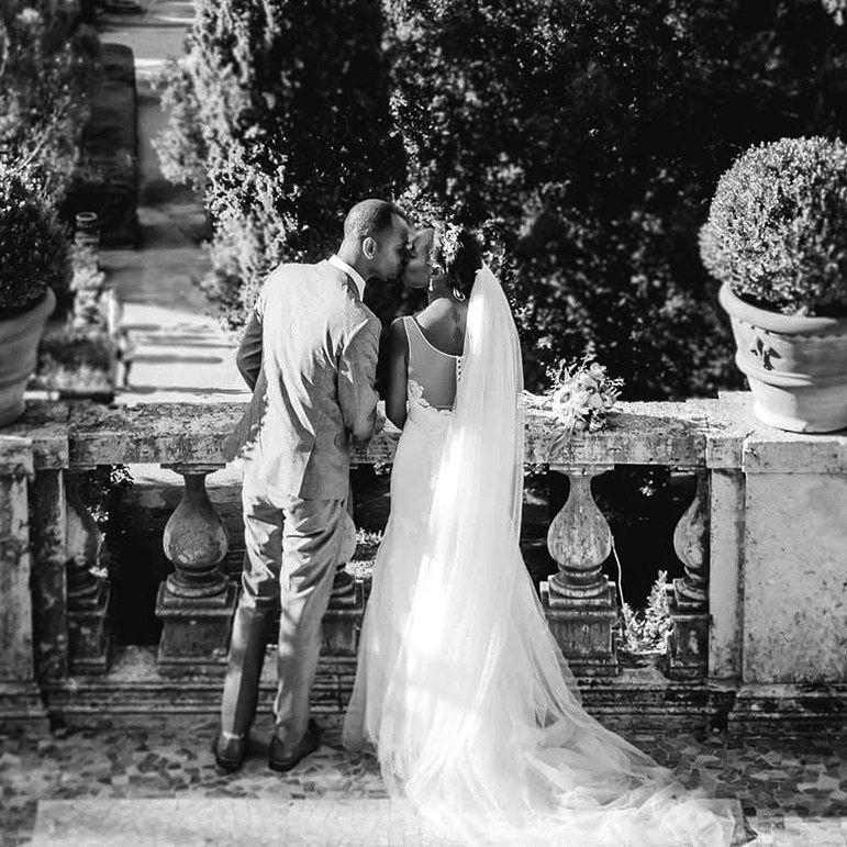 Couple sharing a kiss on a stone terrace, with the bride’s long veil flowing behind her.
