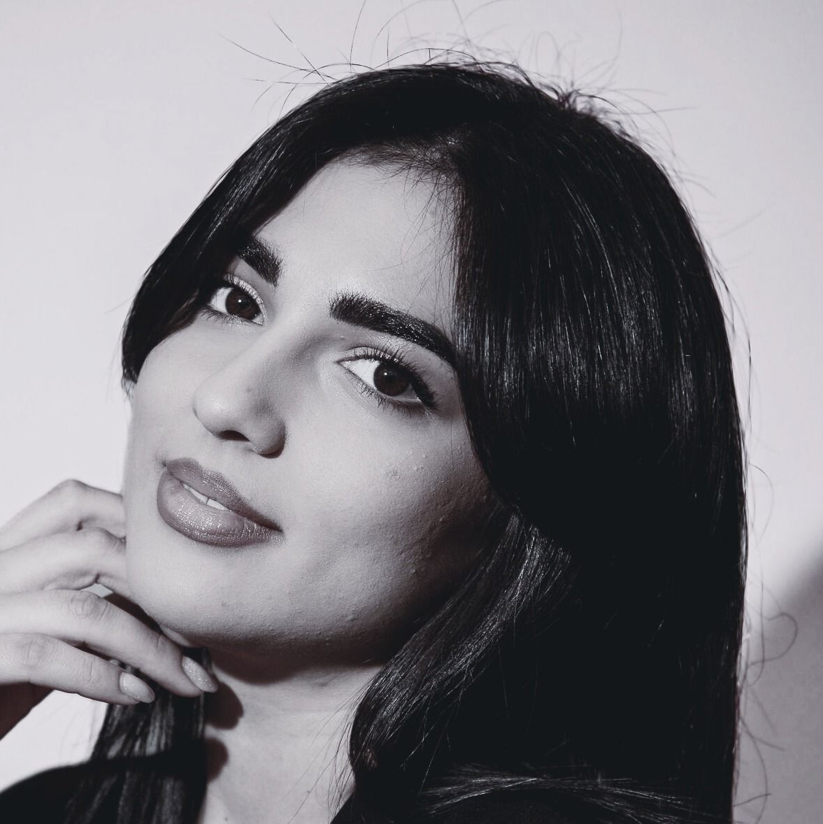 Black-and-white portrait of a person with dark hair, resting their hand near their chin and gazing at the camera