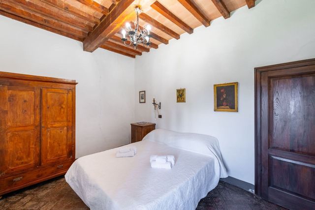 Camera da letto rustica con copriletto bianco, travi in ​​legno, armadio e porte in legno scuro.