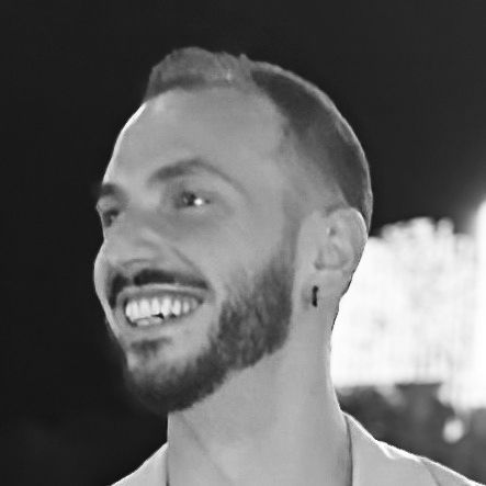 Smiling bearded man in profile at night, with a blurred bright background