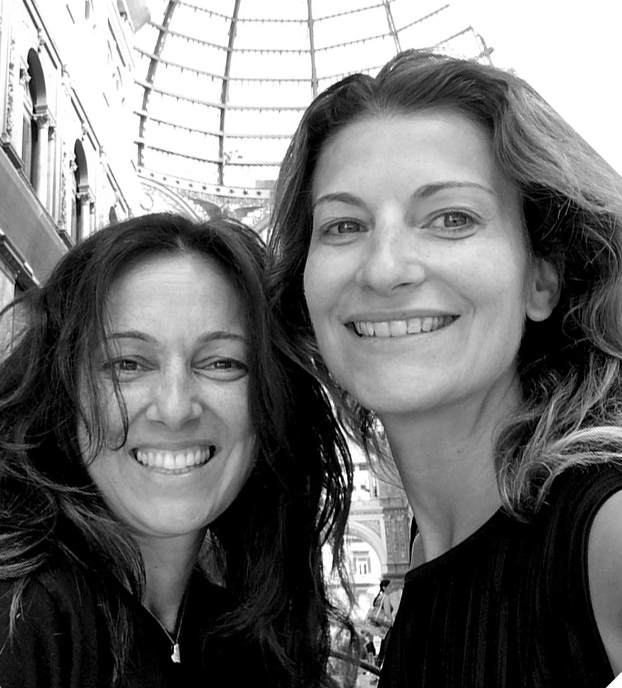 Two smiling people pose under a glass-roofed walkway in black-and-white.