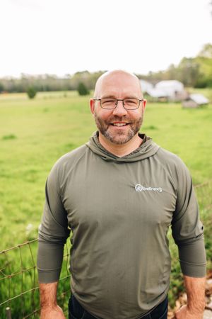 A man with a beard and glasses is standing in front of a grassy field.