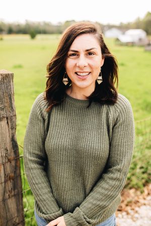 A woman in a green sweater is standing in a field.