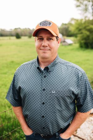 A man wearing a hat and a blue shirt is standing in a field.