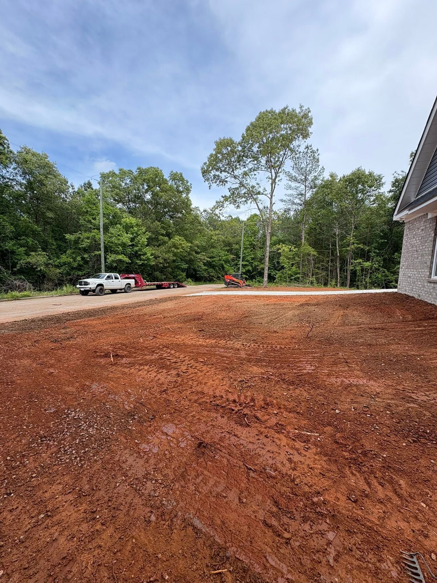 Freshly mulched yard beside a stone house, with trees and parked cars under a blue sky