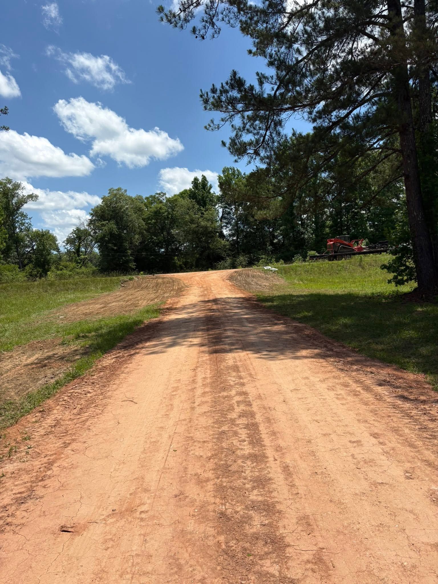 Sandy dirt road curving through green trees under a bright blue sky with clouds