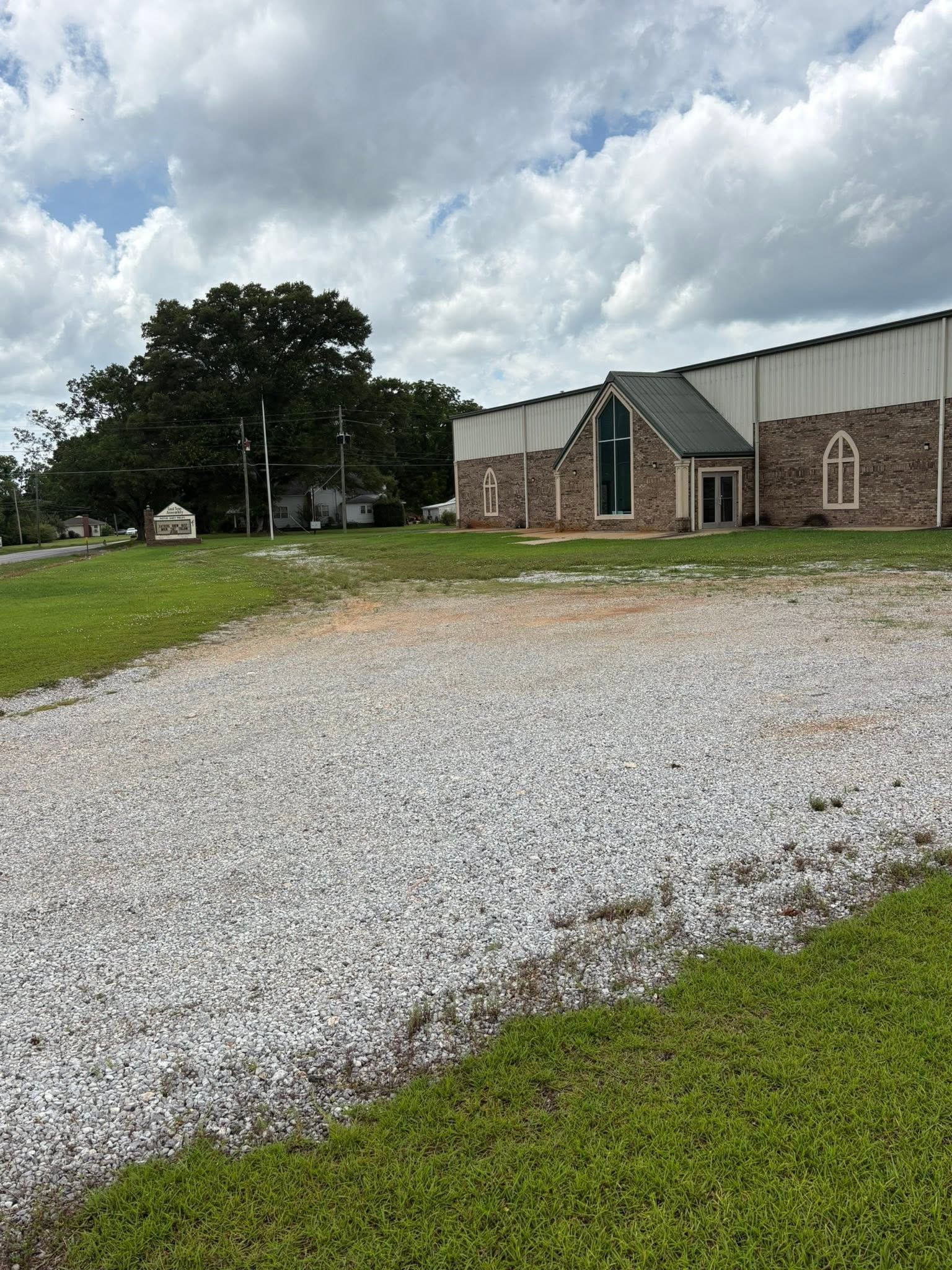 Gravel driveway beside a brick building and trees under a cloudy sky