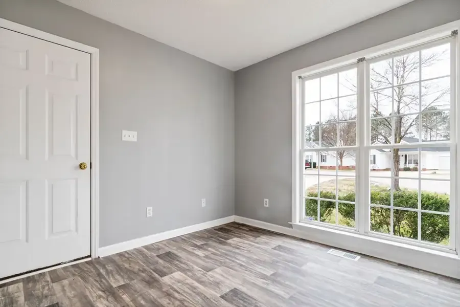 Empty gray room with white closet doors, wood floor, and large window