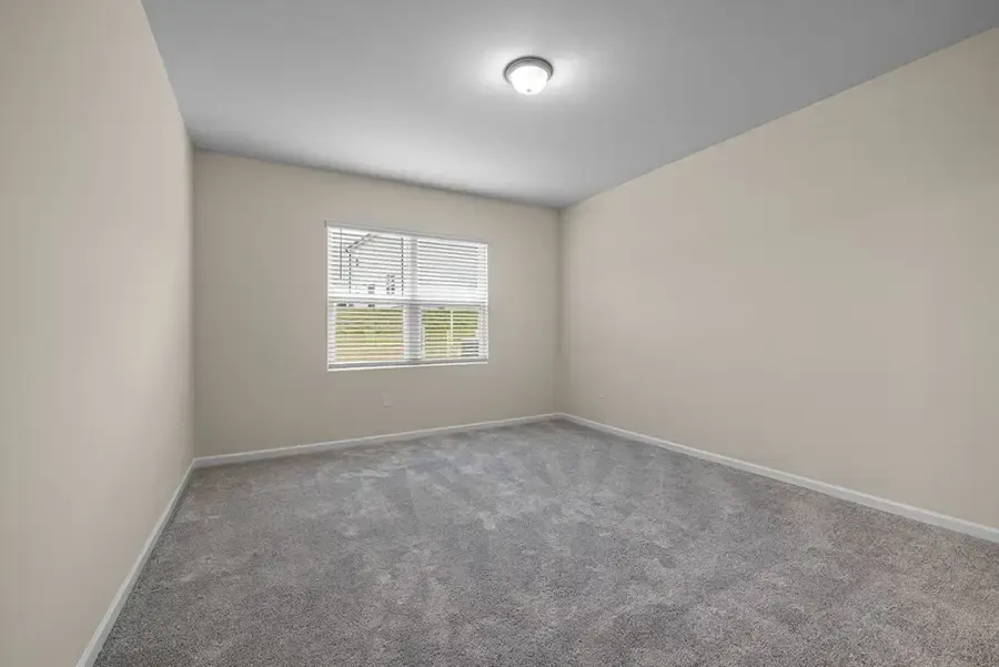 Empty beige bedroom with gray carpet and a window letting in daylight