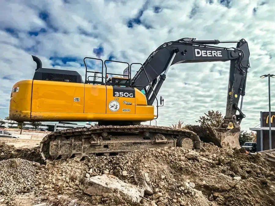 Yellow John Deere excavator digging dirt at a construction site under a cloudy sky