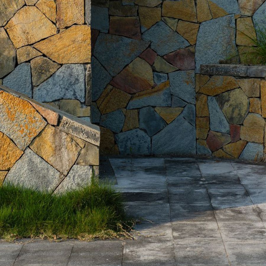 Colorful stone wall with a paved entryway and a strip of grass at the bottom left