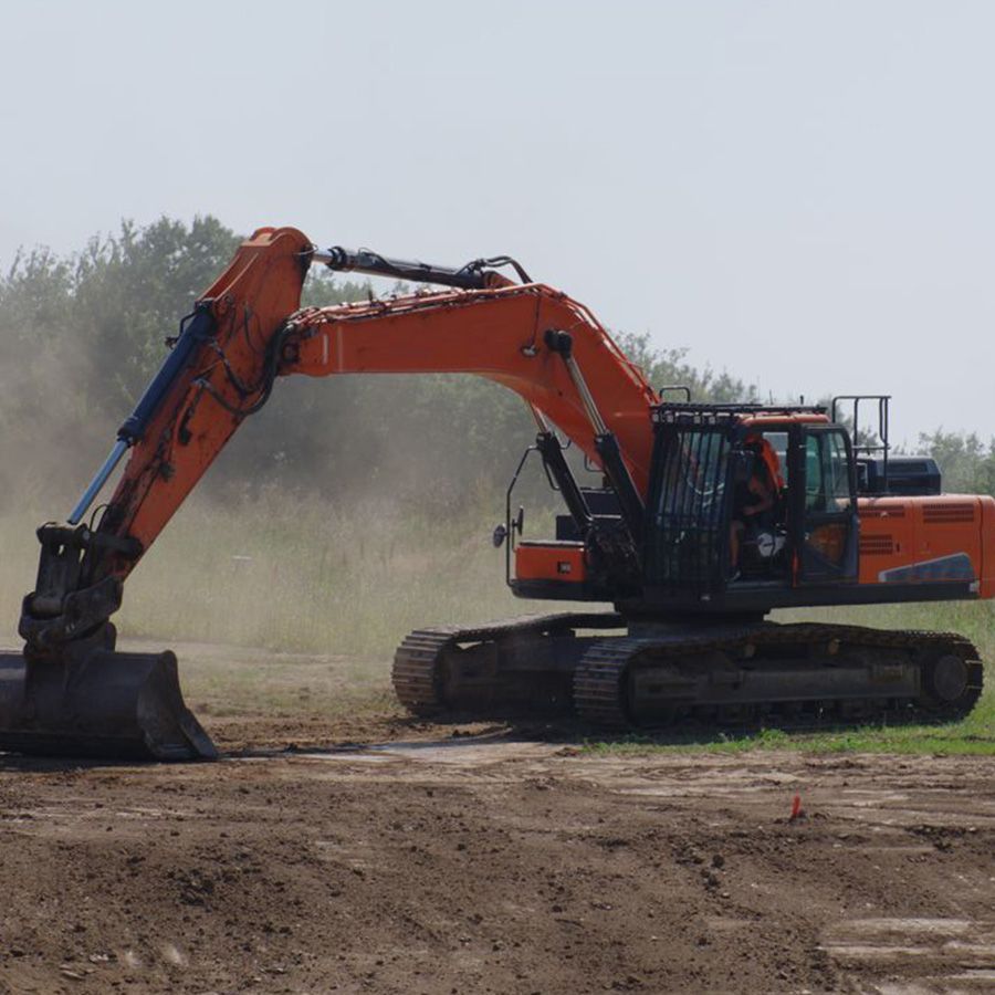 Orange excavator on tracks digging in a dusty dirt field