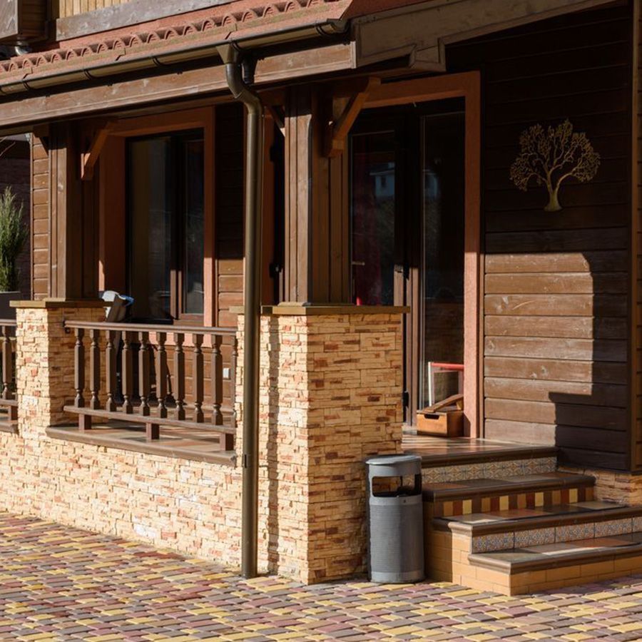 Wooden porch with brick columns, steps, and a small trash bin beside a house.