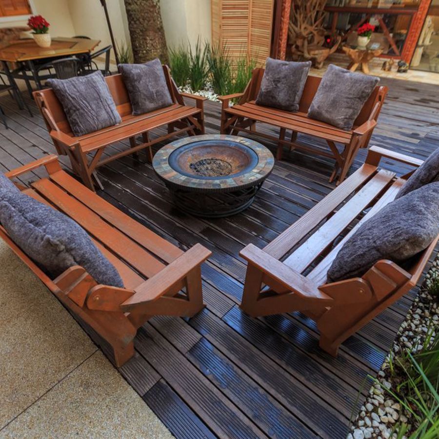 Outdoor wooden patio seating set arranged around a round fire pit on a dark deck.