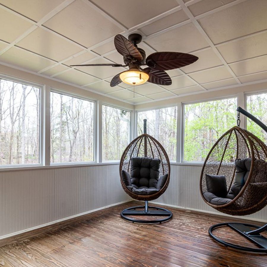 Sunroom with two hanging egg chairs, wood floor, and ceiling fan under large windows