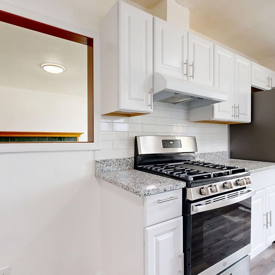 Bright white kitchen with a stainless steel gas range, granite countertop, and subway tile backsplash