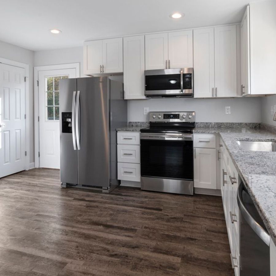 Modern kitchen with stainless steel appliances, white cabinets, granite counters, and dark wood flooring