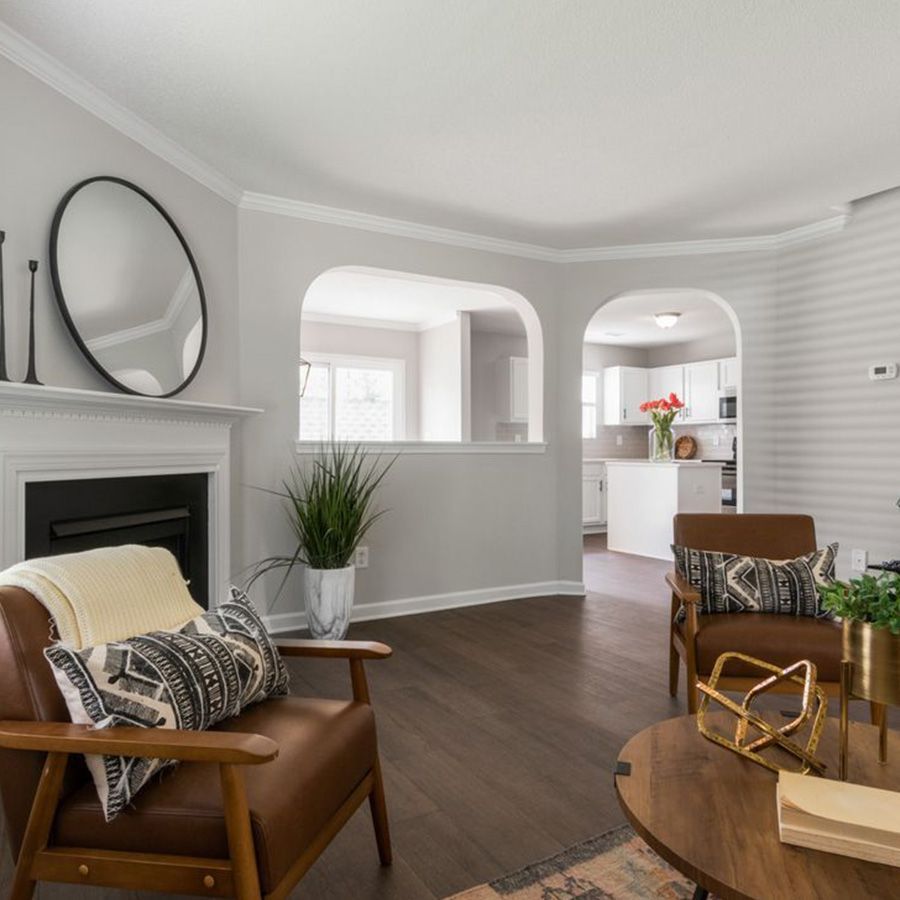 Bright, modern living room with fireplace, brown leather chair, round mirror, and arched openings to the kitchen.