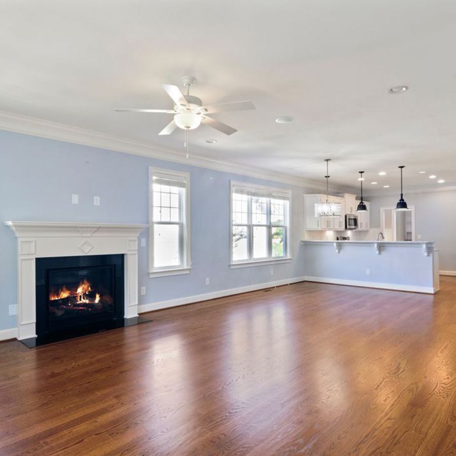 Bright empty living room with fireplace, hardwood floors, ceiling fan, and open kitchen counter