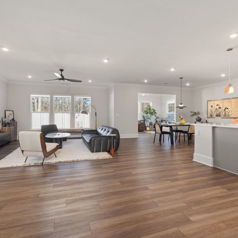 Bright open-plan living room and kitchen with wood floors, gray sofa, dining table, and pendant lights