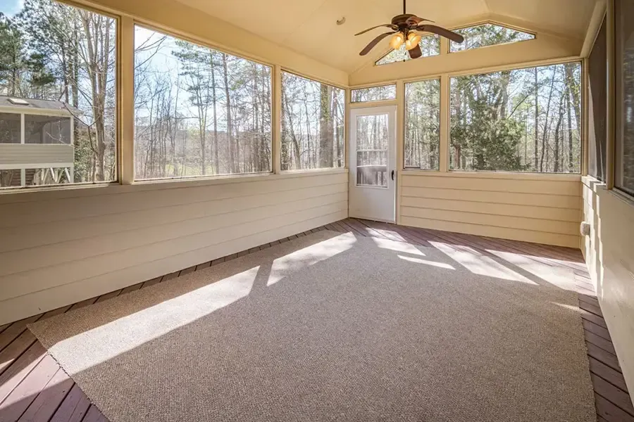 Sunroom with large windows, beige walls, carpeted floor, and ceiling fan in daylight