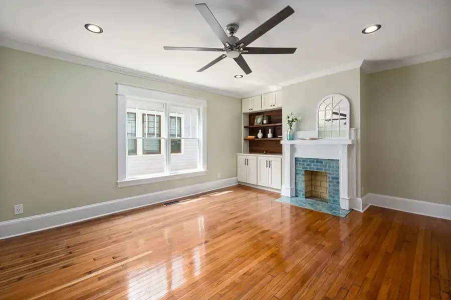 Bright empty living room with hardwood floors, gray walls, fireplace, built-ins, and ceiling fan