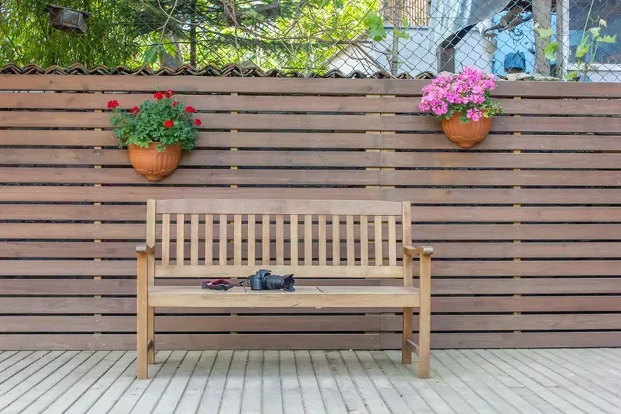 Wooden bench against a slatted fence with hanging flower baskets on a decked patio