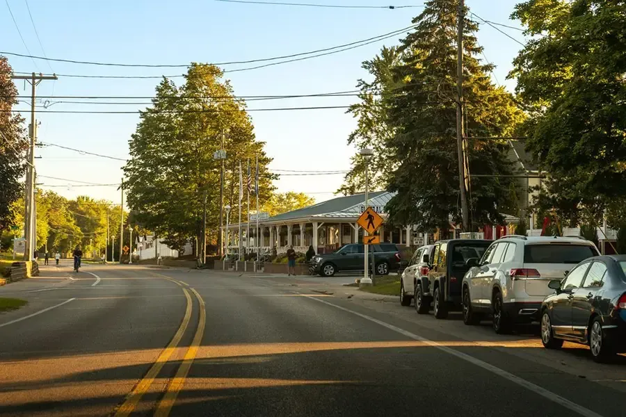 Tree-lined suburban street with parked cars and houses at sunset