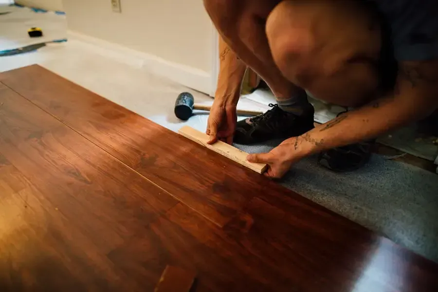 Person installing wood flooring with a tape measure in a home interior
