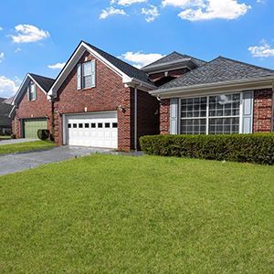 Brick suburban house with a white garage, large windows, and a green lawn under a blue sky