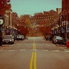 Empty autumn street with yellow center lines, parked cars, and storefronts under warm lights
