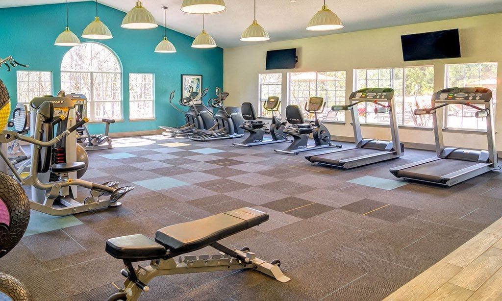 Gym with exercise equipment and windows. Floor tiles, teal wall, and hanging lights.