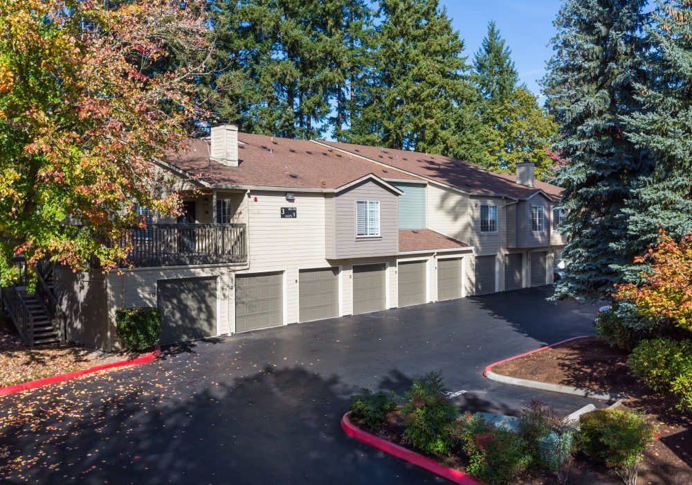 Exterior view of a townhouse-style multifamily building with attached garage doors and surrounding trees at Sofi at Murrayhill, offers apartments for rent in Beaverton, OR.