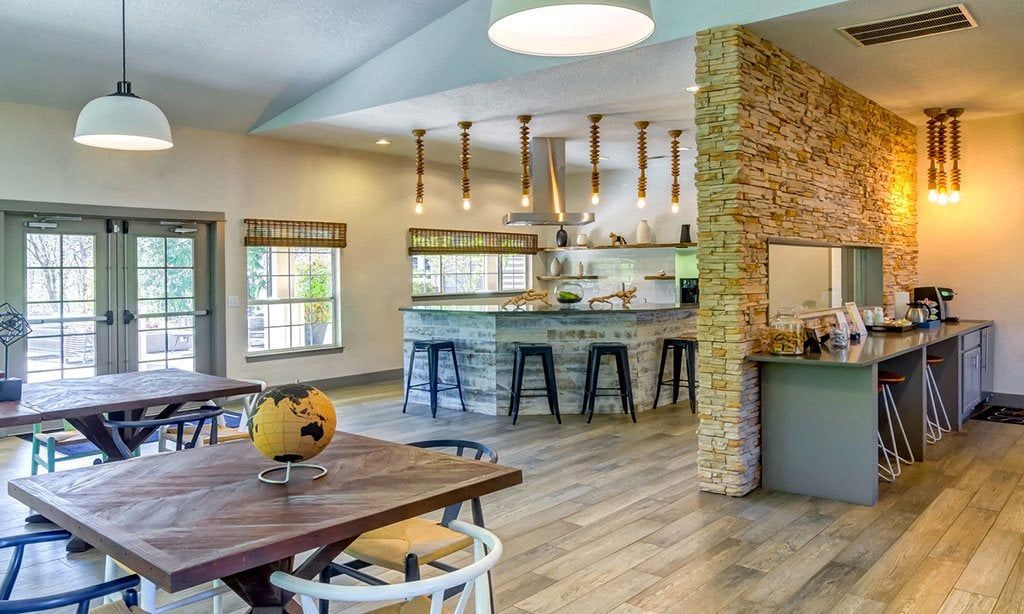 Interior of a community lounge with a bar, stone wall, and wooden tables at Sofi at Murrayhill, offers apartments in Beaverton, OR.
