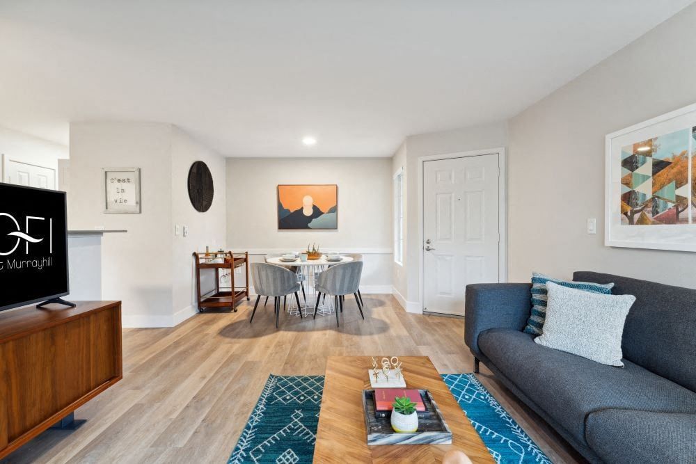 Living room in a modern apartment with gray sofa, coffee table, TV, and dining area at Sofi at Murrayhill, offers apartments near Washington Square Mall.