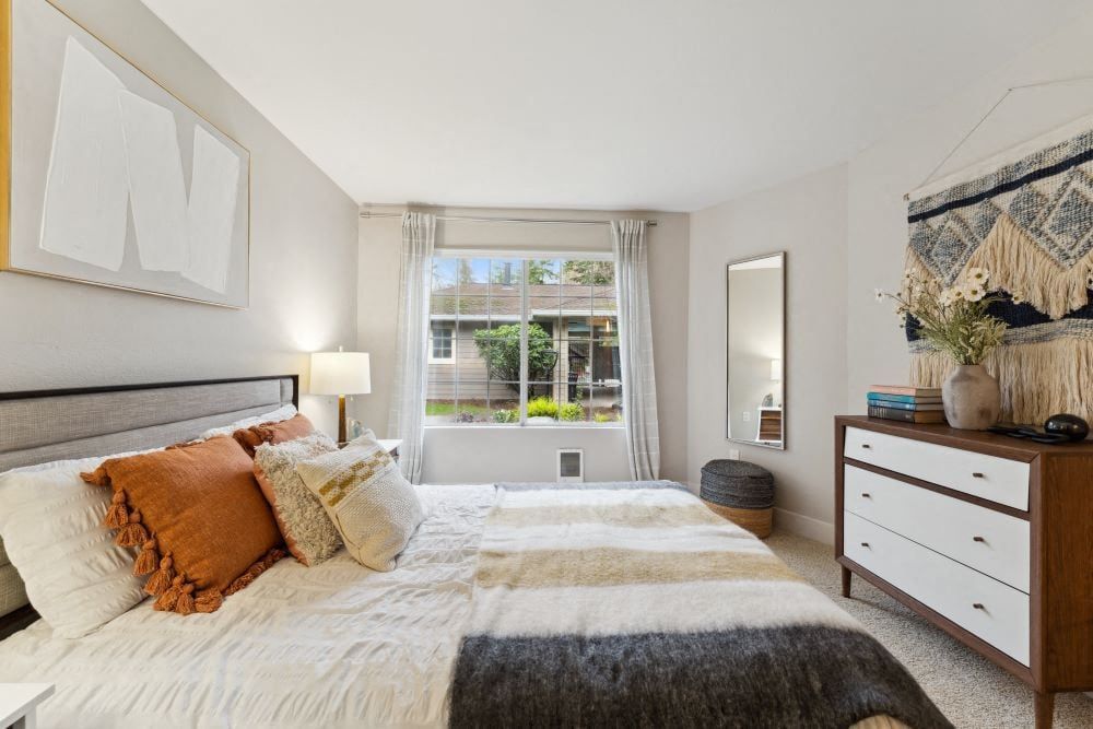 Bedroom interior with a window view, bed with pillows, and a dresser at Sofi at Murrayhill, offers apartments near Washington Square Mall.