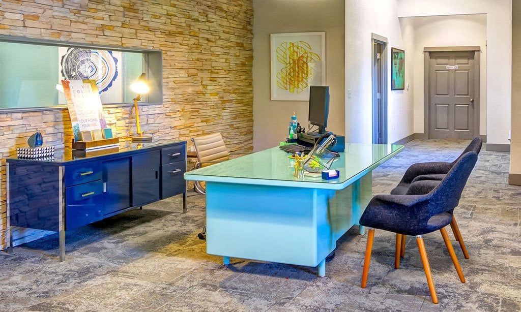 Modern apartment community lobby with a glass-topped reception desk, blue cabinetry, and seating at Sofi at Murrayhill, offers apartments in Beaverton, OR.