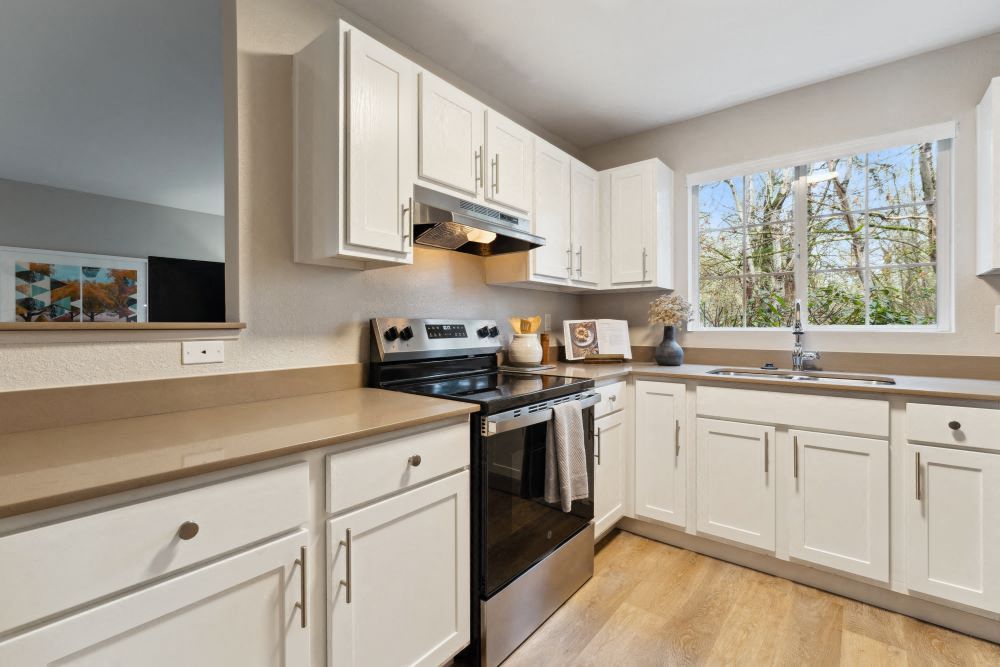 Bright white kitchen with white cabinets, stainless stove, and a large window overlooking trees at Sofi at Murrayhill, offers apartments in Beaverton, OR.
