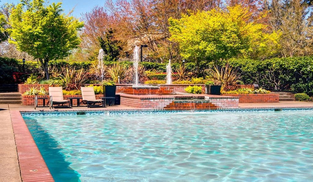 Pool with turquoise water, red brick edge, fountains, and trees in background.