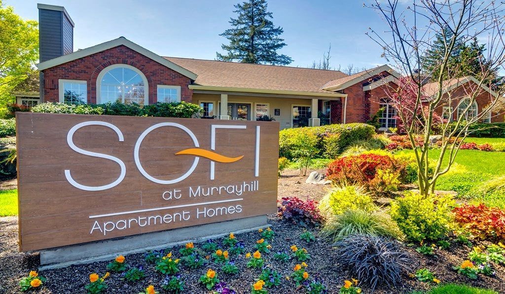 Sign for SOFI on Murphy apartments with building in the background. Brown sign, red brick building, green grass.