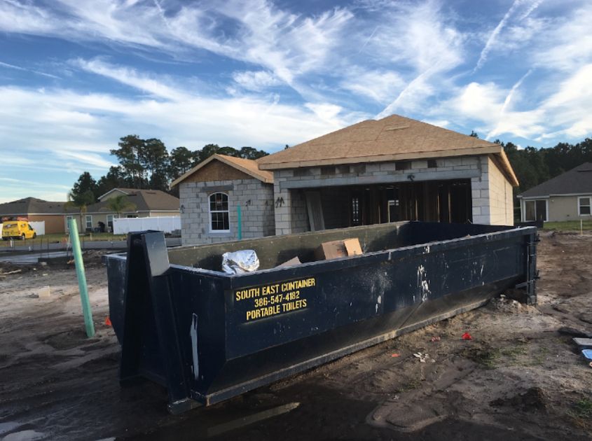 A dumpster is sitting in front of a house under construction.