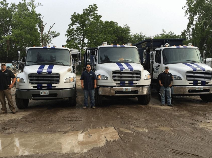 Three men are standing in front of a row of dump trucks.