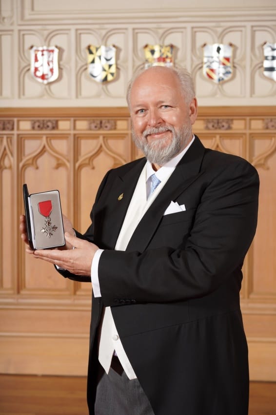 Andrew Taee accepts a red and silver medal MBE