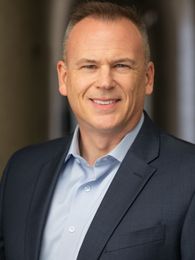 A man in a suit and blue shirt is smiling for the camera.